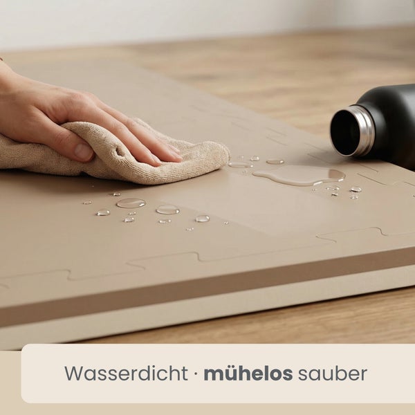 Hand wischt Wassertropfen von einer wasserdichten, steckbaren Bodenmatte mit einem Tuch ab. Mühelos sauber.