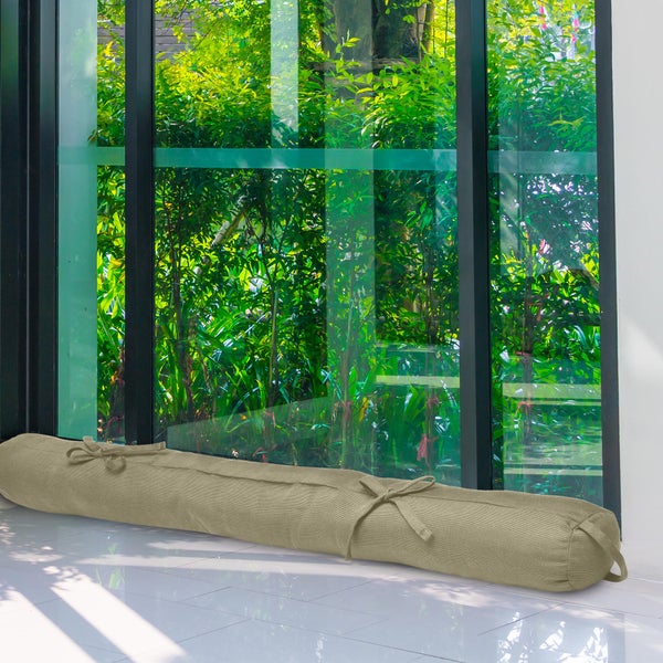 Zugluftstopper aus Stoff in Beige vor einem bodentiefen Fenster mit Blick in den Garten.