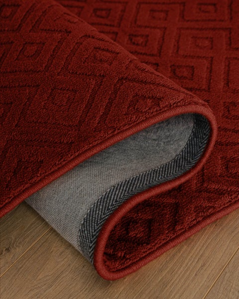 Roter Teppich mit geometrischem Rautenmuster, Detailansicht mit umgeschlagener Ecke auf Holzboden.