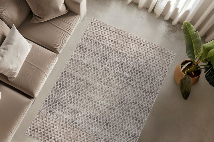 Wohnzimmer mit einem rechteckigen Teppich mit geometrischem Dreiecksmuster vor einem Sofa neben einer Zimmerpflanze auf einem Betonboden.