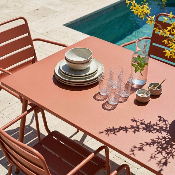 Moderner Garten-Essplatz mit Metalltisch und Stühlen in Terrakotta auf einer Steinterrasse am Pool, gedeckt mit Geschirr und Gläsern.