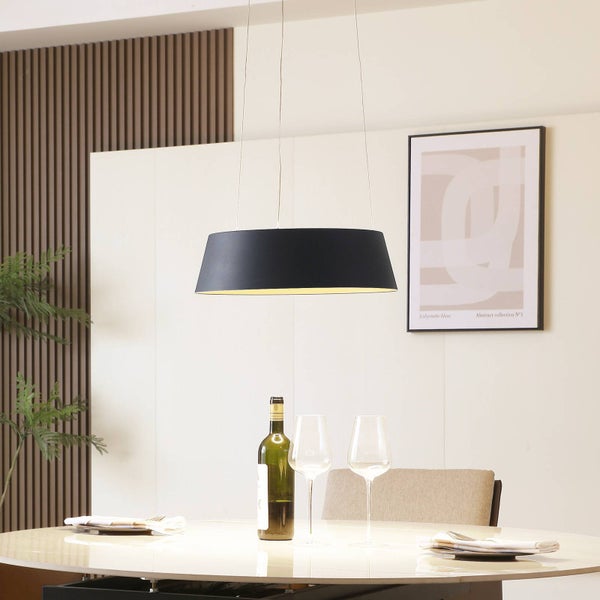 Moderne Pendelleuchte mit schwarzem Schirm und goldfarbener Innenseite über einem gedeckten Esstisch in einem hellen Raum.