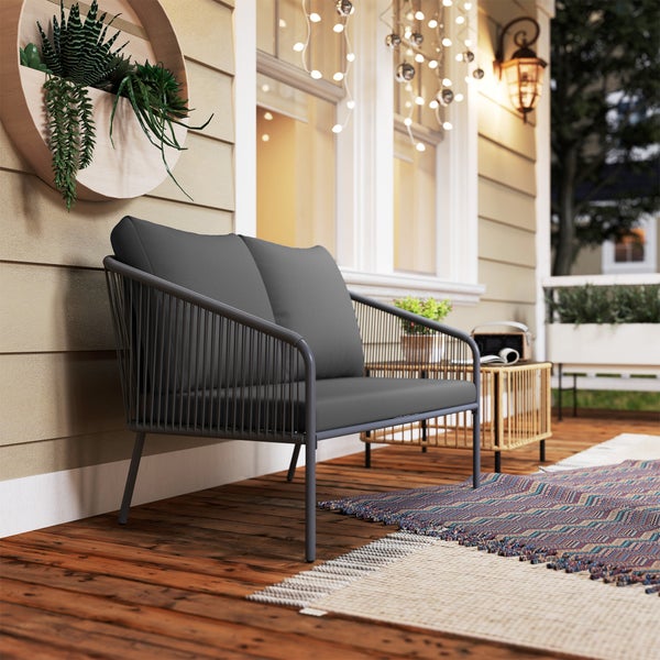 Modernes Gartensofa mit Seil-Design und grauen Kissen auf einer Holzterrasse mit Outdoorteppich, Beistelltisch und Wandbepflanzung.