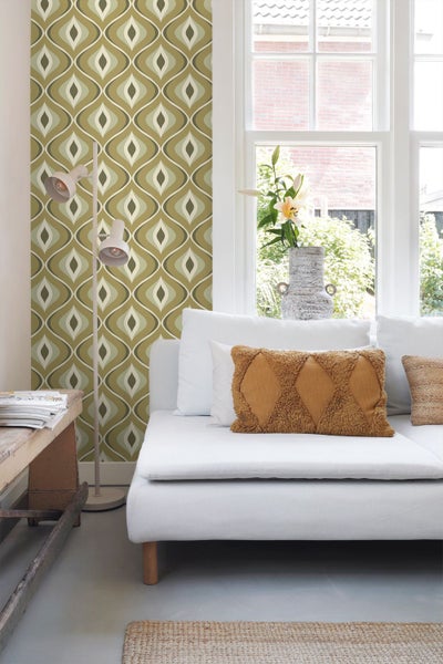 Vliestapete mit geometrischem Retro-Muster in einem hellen Wohnzimmer mit weißem Sofa und Stehlampe.