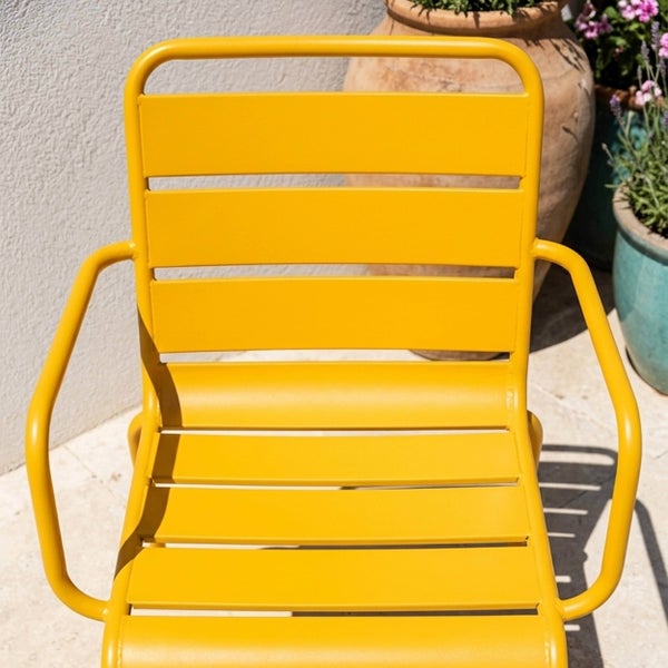 Gelber Gartenstuhl aus Metall mit Armlehnen und Lamellendesign, auf einer hellen, organisierten Terrasse neben Pflanzgefäßen.