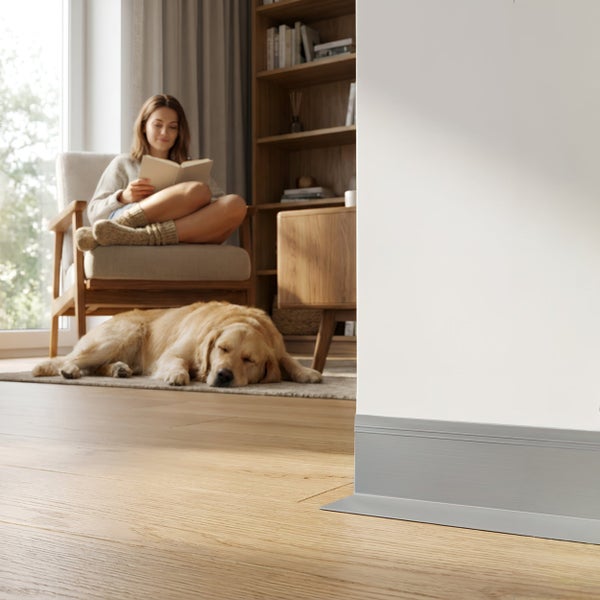 Moderne Fußleiste in einem hellen Wohnraum mit Holzboden, einer lesenden Frau und einem schlafenden Hund im Hintergrund.