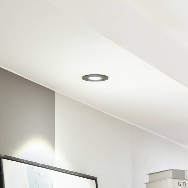 Moderner, heller Raum mit einem runden, schwarzen Einbaustrahler in einer weißen Decke, der eingeschaltet ist und Licht abgibt.