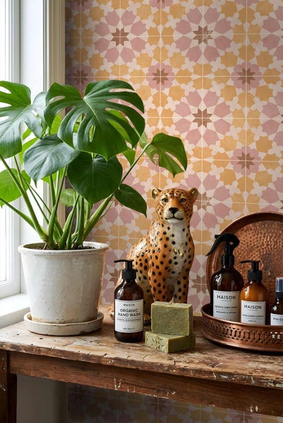 Szene mit gemusterten Wandfliesen, Monstera-Pflanze, Leopardenfigur und Pflegeprodukten mit Maison Logo auf einem Holztisch.