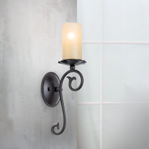 Wandleuchte im Landhausstil mit geschwungenem Metallarm und zylindrischem Leuchtenglas zur stimmungsvollen Beleuchtung.