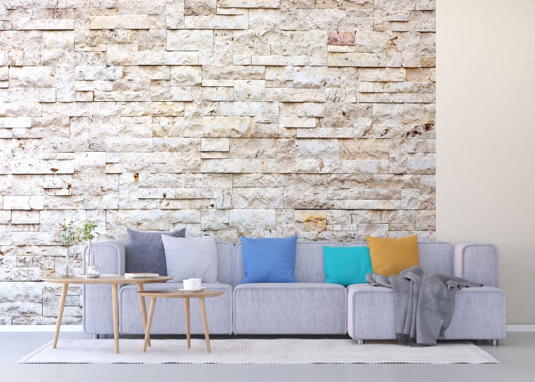 Wohnzimmer mit grauer Couch, Kissen und Steinwand