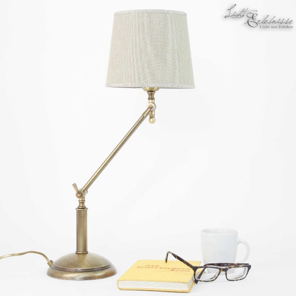 Verstellbare Tischleuchte aus Metall mit Stoffschirm neben Buch, Brille und Tasse