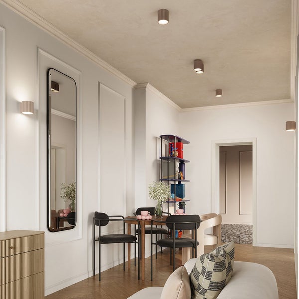 Hell gestalteter Wohnraum mit modernen Deckenstrahlern und Wandleuchten, einem hohen Spiegel und einem Esstisch mit schwarzen Stühlen.