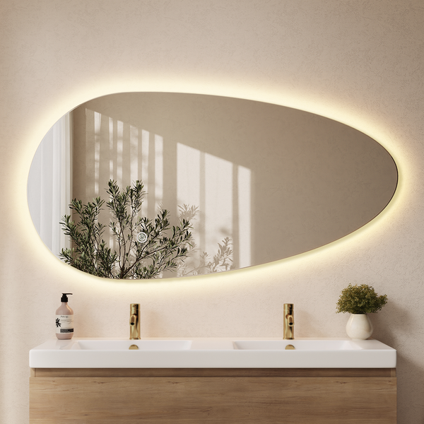 Organisch geformter Badezimmerspiegel mit indirekter LED Beleuchtung über einem Doppelwaschtisch mit Holzunterschrank und Armaturen.