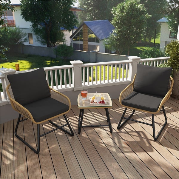 Gartenmöbelset mit zwei Korbstühlen, schwarzen Kissen und Tisch mit Glasplatte auf einer Terrasse