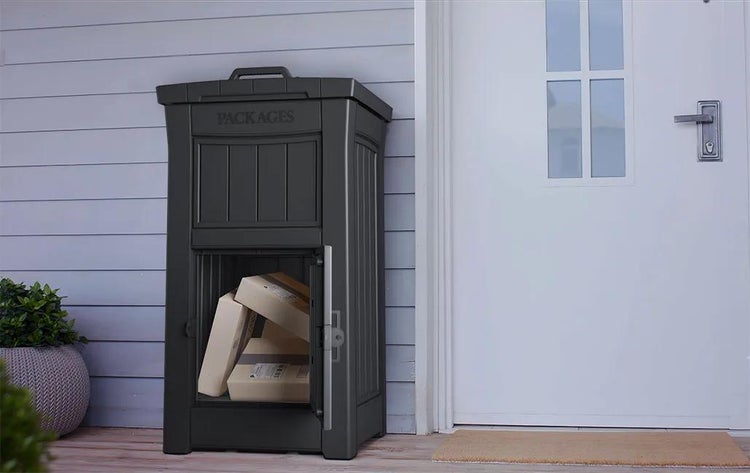 Dunkelgraue Paketbox mit geöffneter Tür und Paketen im Inneren, platziert neben einer weißen Haustür.