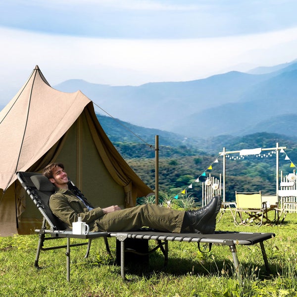 Ein Mann entspannt auf einer klappbaren Campingliege vor einem Tipi-Zelt in einer Berglandschaft.