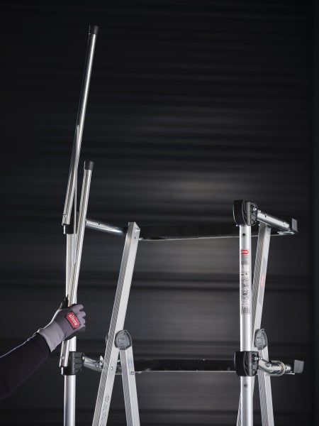 Eine Aluminium-Arbeitsbühne mit einer Person, die die Holmsicherung einstellt