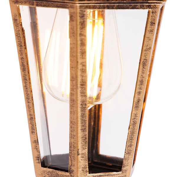 Nahaufnahme einer Außenlaterne mit verwittertem goldfarbenem Metallrahmen, Klarglas und leuchtendem LED-Filament-Leuchtmittel.