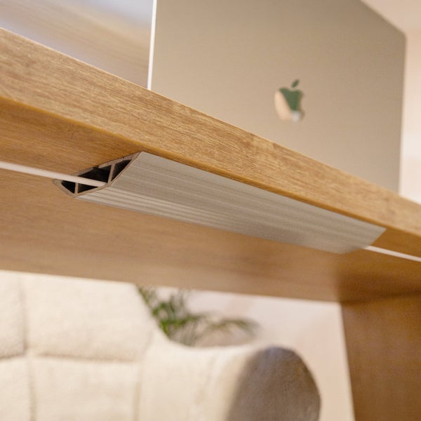 Kabelkanal zur Montage unter einer Schreibtischplatte aus Holz mit einem geführten Kabel und einem Laptop im Hintergrund.