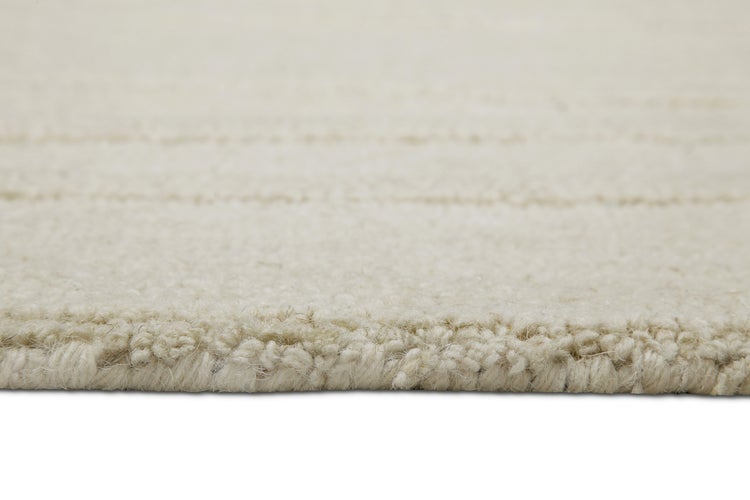 Nahaufnahme der strukturierten Oberfläche und der Kante eines Hochflor-Teppichs mit horizontalen Linien.