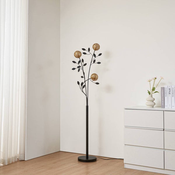 Dekorative Stehlampe mit Blattdesign und drei kugelförmigen Lampenschirmen neben einer Kommode.