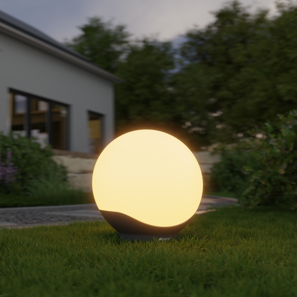 Leuchtende Kugelleuchte für den Garten auf einer Rasenfläche vor einem Wohnhaus und Bäumen.