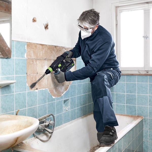 Handwerker stemmt mit einem Bohrhammer Fliesen von einer Badezimmerwand.
