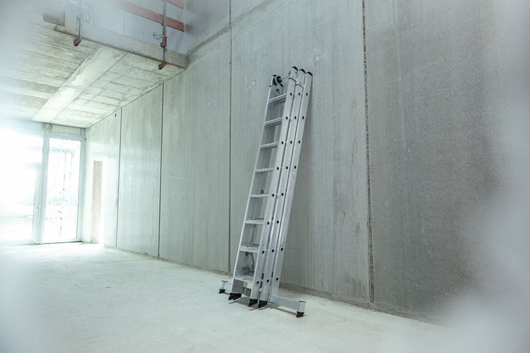 Mehrzweckleiter aus Aluminium an einer Betonwand in einem Rohbau