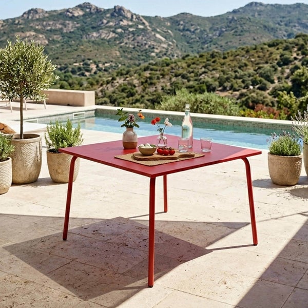 Moderner roter quadratischer Gartentisch aus Metall auf einer hellen Steinterrasse mit Pool, Bergpanorama und verschiedenen Kübelpflanzen.