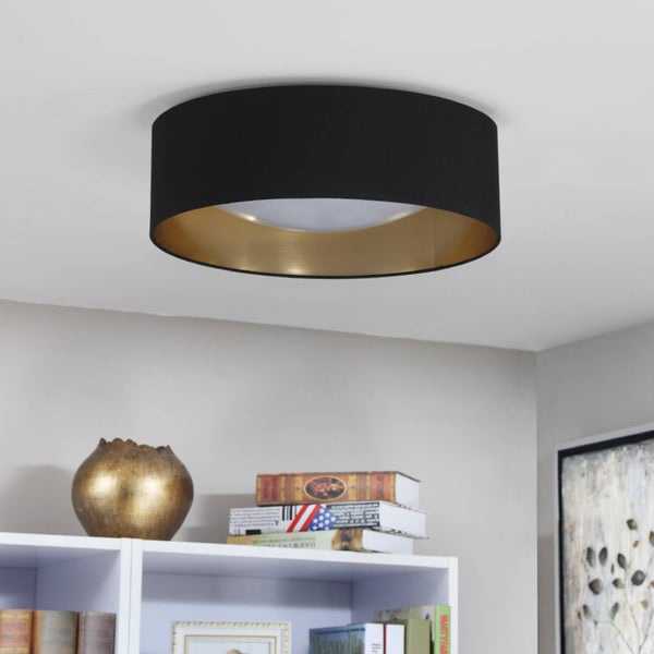 Runde Deckenleuchte mit schwarzem Textilschirm und goldfarbener Innenseite montiert an einer weissen Decke über einem Regal.