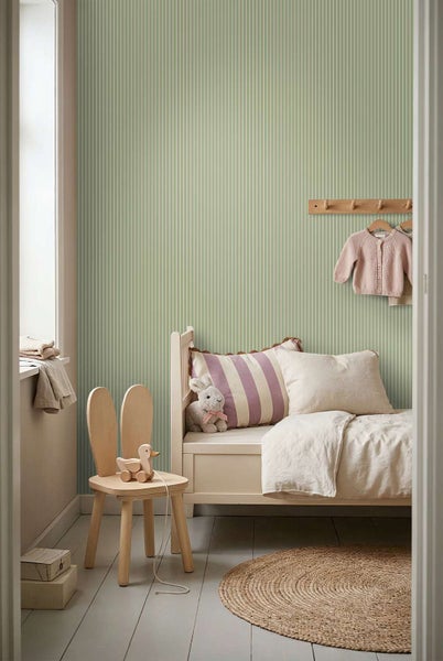 Ein Kinderzimmer mit gestreifter Tapete, einem hellen Kinderbett, einem Holzstuhl in Hasenform und einem runden Jute Teppich.