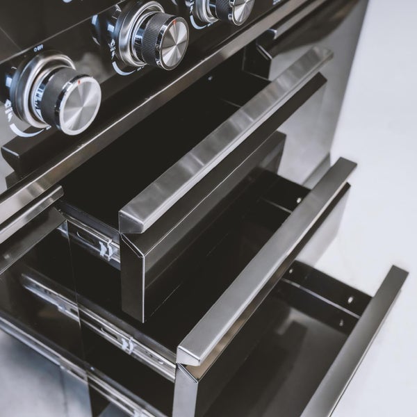 Nahaufnahme eines schwarzen Gasgrills mit drei geöffneten Schubladen, Edelstahlgriffen und oben liegenden Drehreglern.
