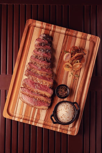 Holzschneidebrett mit aufgeschnittenem Steak, Gewürzen und Zwiebeln