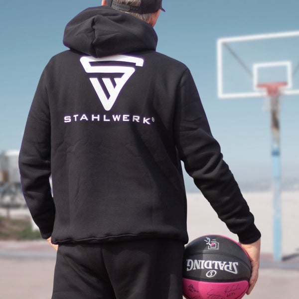 Person im schwarzen Stahlwerk Kapuzenpullover mit Basketball vor Basketballkorb