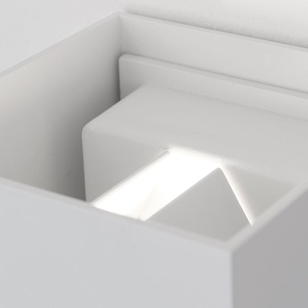 Nahaufnahme einer weißen würfelförmigen Wandleuchte mit leuchtendem LED-Modul im Inneren.