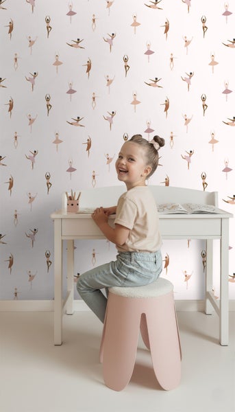 Mädchen sitzt an einem weißen Schreibtisch vor einer Tapete mit Ballerina Muster