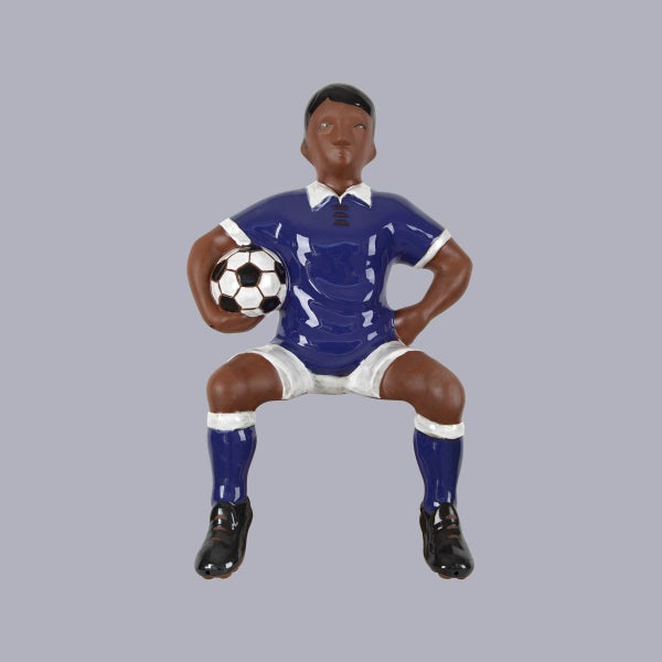 Sitzende Gartenfigur eines Fußballspielers mit Fußball in blauem Trikot und weißen Hosen.
