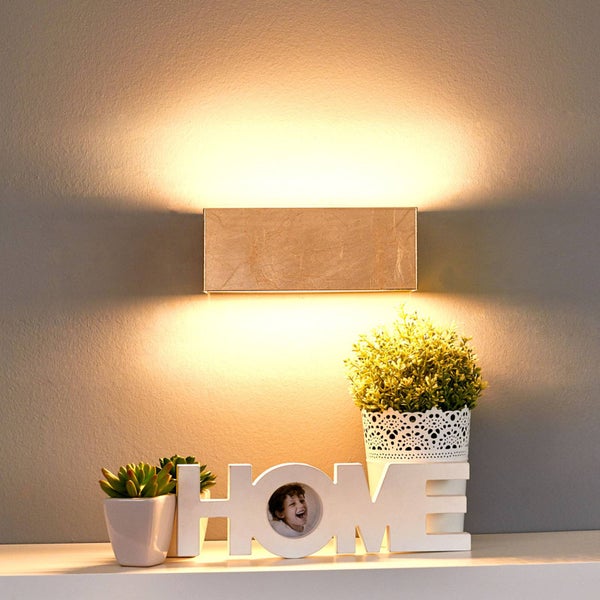 Rechteckige Wandleuchte in Goldoptik mit Licht nach oben und unten über einem Regal mit Pflanzen und dekorativem Schriftzug.