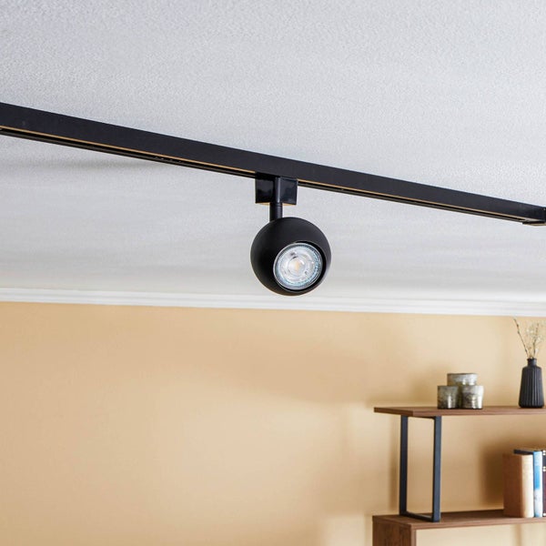 Schwarzes Schienensystem mit kugelförmigem Strahler an einer Zimmerdecke in einem modernen Raum.