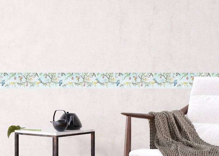 Selbstklebende Tapetenbordüre mit Vogel und Zweigmuster auf einer hellen Wand hinter einem Sessel und Beistelltisch.