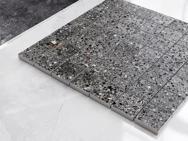 Quadratisches Mosaik aus Feinsteinzeug in Terrazzo-Optik mit grauen und schwarzen Fragmenten.