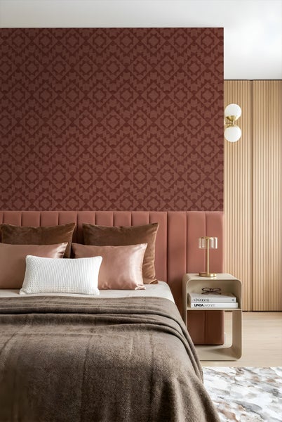 Modernes Schlafzimmer mit geometrisch gemusterter Vliestapete hinter einem gepolsterten Kopfteil und einem Nachttisch mit goldener Lampe.