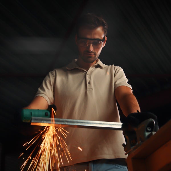 Mann mit Schutzbrille schneidet Metall mit einem Trennschleifer, wodurch Funken entstehen.