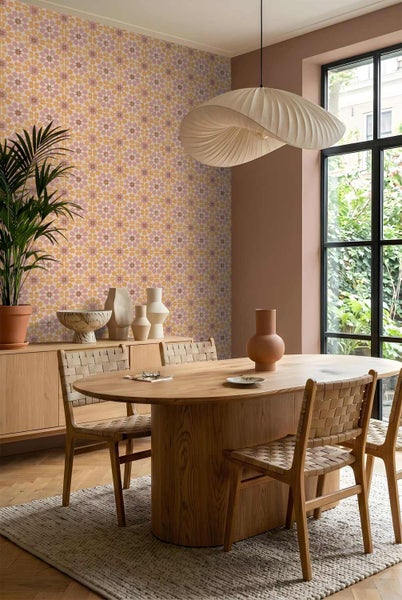 Modernes Esszimmer mit ovalem Holztisch, Geflechtstühlen und einer Wand mit geometrisch gemusterter Tapete. Inklusive großer Pendelleuchte.