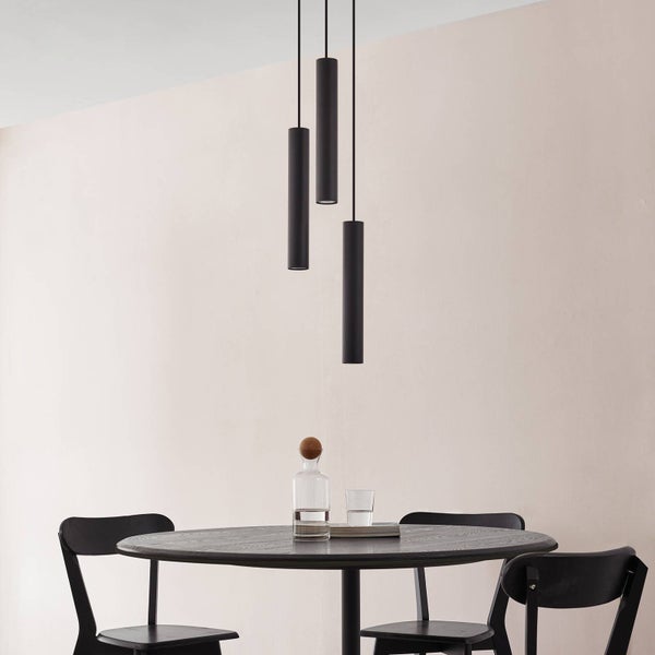 Drei schwarze Pendelleuchten über einem Esstisch mit Stühlen