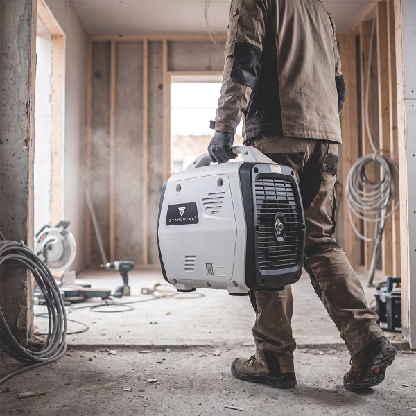 Tragbarer STAHLWERK Inverter Stromerzeuger wird auf einer Baustelle von einer Person getragen.