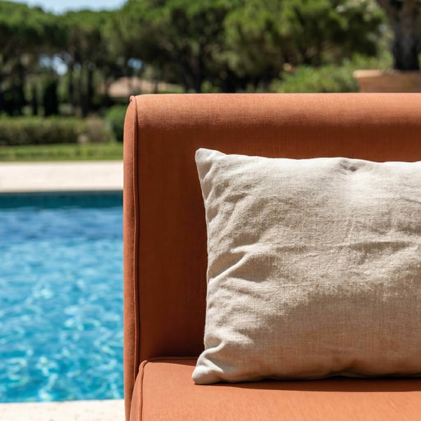 Nahaufnahme eines Gartenmöbels mit terrakottafarbenem Bezug und beigem Zierkissen im Außenbereich neben einem Pool.