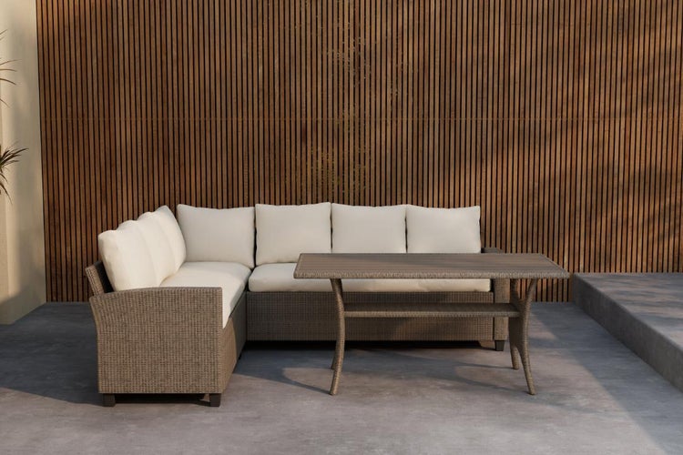 Gartenlounge aus grauem Polyrattan mit Ecksofa, cremefarbenen Kissen und rechteckigem Tisch vor einer Holzlamellenwand.