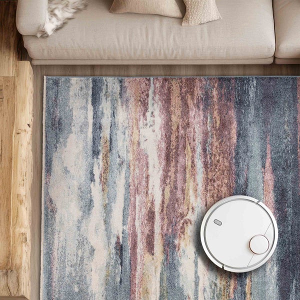 Ansicht von oben: Teppich mit Abstraktem Muster, Saugroboter und Teil eines Sofas.