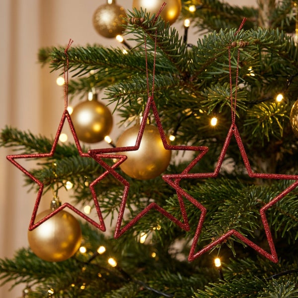 Drei sternförmige Weihnachtsanhänger mit Glitzer am Weihnachtsbaum mit goldener Kugeldekoration und Lichterkette.